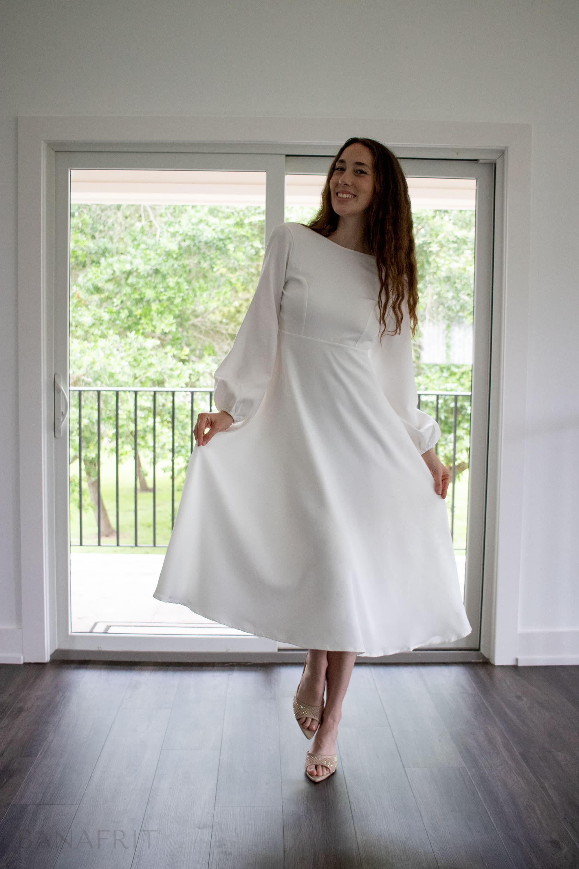 Fine art portrait — woman in white long-sleeve midi dress, spinning in natural light near glass door